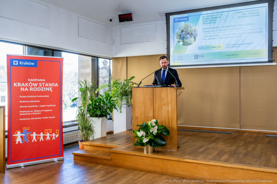 Prezydent Krakowa Aleksander Miszalski przemawia przy mównicy otwierając konferencję. W tle plansza wydarzenia.