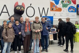 Targi BOOKGAME 21.03.2025 Uczestnicy na tle banneru reklamowego Targi Gier BookGame Kraków 2025