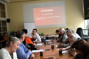 Procesy poznawcze 24.03.2025 Kilkoro mieszkańców siedzi przy długim stole, piszą coś na kartkach.