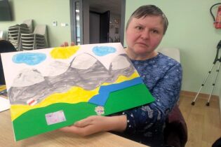 Warsztaty plastyczne 26.03.2025 Mieszkanka trzyma w rękach dużą kartkę z kolorową pracą