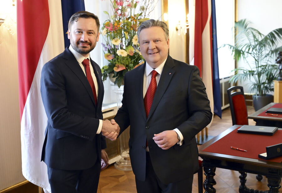Prezydent Krakowa oraz Burmistrz Wiednia stoją obok stołu na którym leżą teczki z dokumentem podpisanej właśnie umowy i ściskają dłonie w serdecznym geście tle flagi Wiednia.