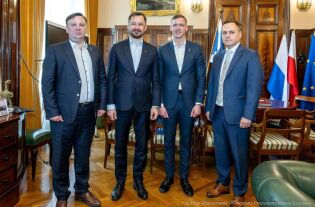 Wizyta Mera Rejonu Wileńskiego Wizyta Mera Regionu Wileńskiego u Prezydenta Krakowa 5 maja 2025 r. Na zdjęciu w gabinecie Prezydenta Krakowa stoją na tle flag i ściany z ciemną boazerią od lewej doradca mera do spraw kultury, Prezydent Aleksander Miszalski, Mer Robert Duchniewicz i Przewodniczący Rady Miasta Krakowa Jakub Kosek.