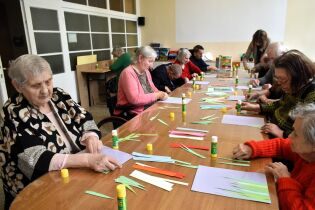 Arteterapia 16.05.2025 Wokół dużego stołu siedzi kilkunastu mieszkańców, sklejają kolorowe paski papieru