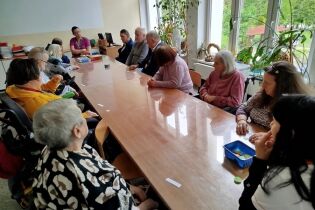 Kalambury 19.05.2025 Kilkunastu mieszkańców siedzi wokół dużego stołu.