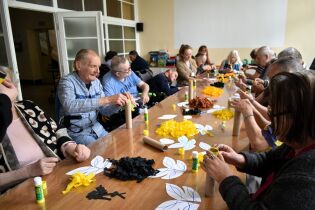 Kreatywny recykling 23.05.2025 Kilkunastu mieszkańców przy długim stole przykleja bibułę do papieru.