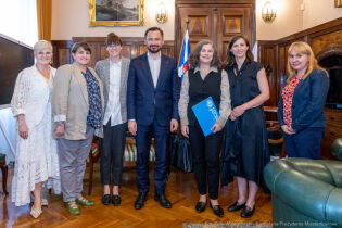 Spotkanie Prezydenta z Koordynatorką Krajową Biura UNICEF ds. Reagowania na Potrzeby Uchodźców w Polsce Zdjęcie grupowe. W gabinecie Prezydenta Krakowa stoi w rzędzie 7 osób. W centrum Prezydent Aleksander Miszalski obok po prawej Nona Zicherman z UNICEF.