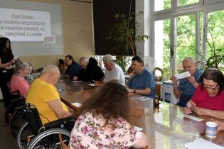 Kilkunastu mieszkańców siedzi przy długim stole.