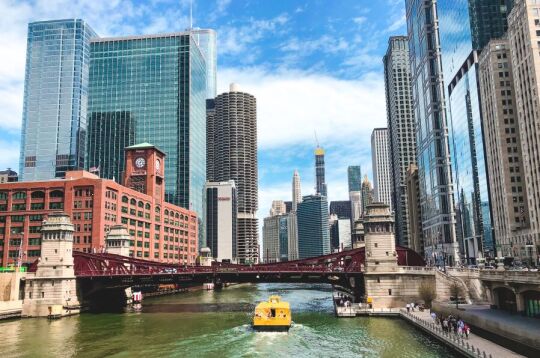 Krajobraz Chicago - wysokie wieżowce, rzeka i łódka z turystami.