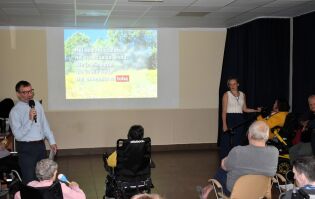 Karaoke 17.07.2025 Zajęcia karaoke dla seniorów w sali. Pan Dyrektor trzyma mikrofon i śpiewa, a na ekranie wyświetlany jest tekst piosenki. Uczestnicy siedzą na krzesłach i wózkach inwalidzkich.