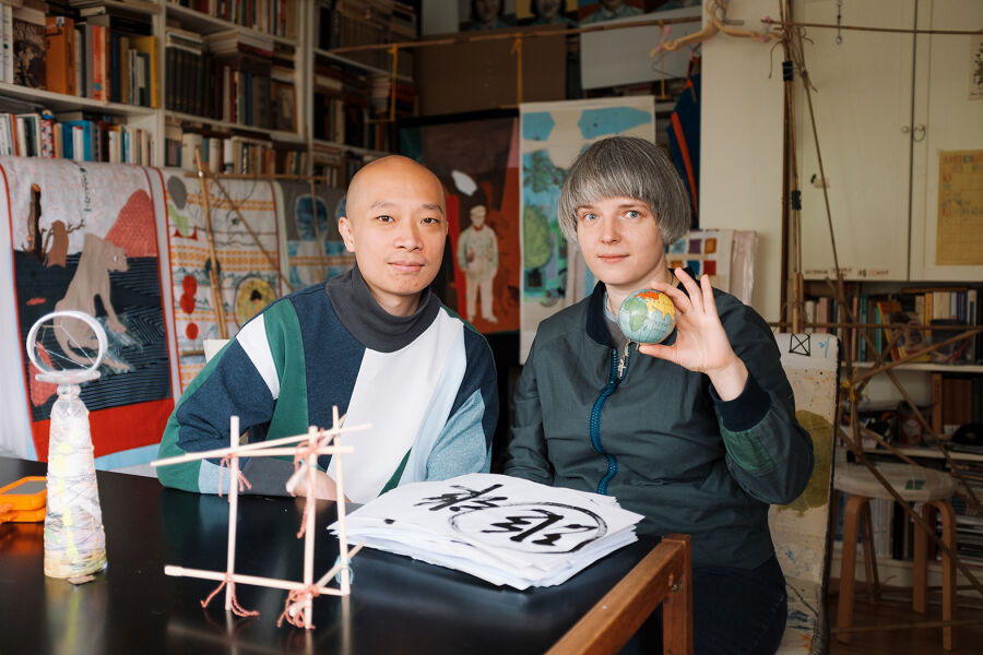 Na fotografii w gabinecie pełnym książek i dzieł artystycznych Maria Stanisława Sala oraz Cheong Kin Man siedzą za stołem. Kobieta trzyma w dłoni piłeczkę-kulę ziemską. 