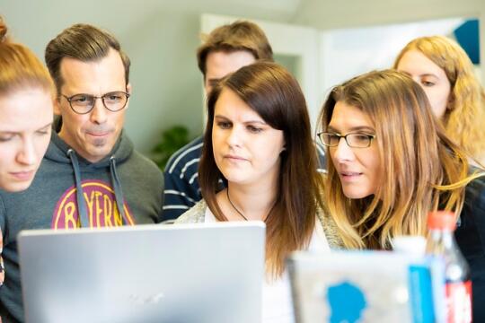 Na zdjęciu widzimy grupę osób wpatrzone w monitor laptopa