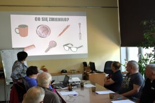Procesy poznawcze 25.08.2025 „Grupa osób siedzi przy stole w sali szkoleniowej i ogląda prezentację wyświetloną na ekranie.
