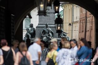 na fotografii turyści przechodzący przez środek Sukiennic na Rynek Główny w stronę pomnika Adama Mickiewicza.   