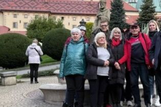 grupa osób stoi na tle klasztoru