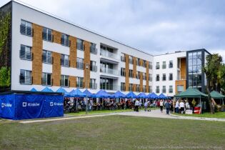 Na zdjęciu namioty ze stoiskami oraz namioty Miasta Krakowa, gdzie siedzą mieszkańcy oraz zaproszeni mieszkańcy z innych DPS-ów w ogrodzie na tle Domu. 