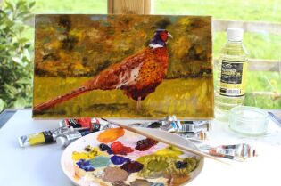 Grafika przedstawia obraz z namalowanym bażantem oraz kolorowe farby.