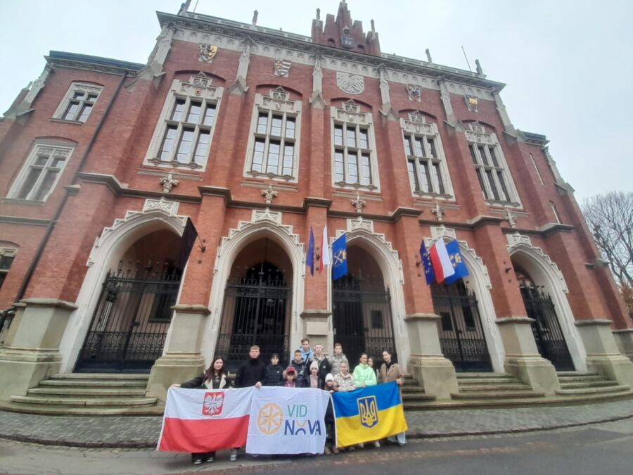 Dzieci z Ukrainy odwiedziły Kraków 11.11.2025. Zdjęcie przedstawia grupę młodych osób z flagami Polski i Ukrainy stojących przed głównym wejściem do gmachu Collegium Novum. 