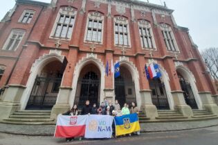 Dzieci z Ukrainy odwiedziły Kraków 11.11.2025. Zdjęcie przedstawia grupę młodych osób z flagami Polski i Ukrainy stojących przed głównym wejściem do gmachu Collegium Novum. 