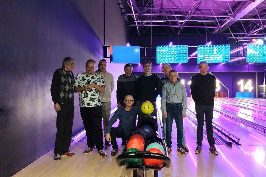Grupa mężczyzn pozuje wspólnie przy torach kręglarskich, przed nimi stoją kolorowe kule do gry.