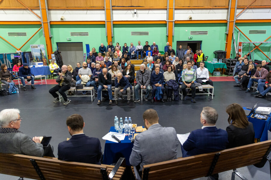 Na zdjęciu widać ludzi siedzących na trybunkach w sali sportowe podczas spotkania w ramach ławki dialogu w Bronowicach.