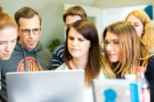 Grafika przedstawia kilka osób, zebranych wokół monitora komputera.