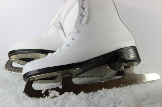 Grafika przedstawia białe łyżwy do jazdy figurowej.