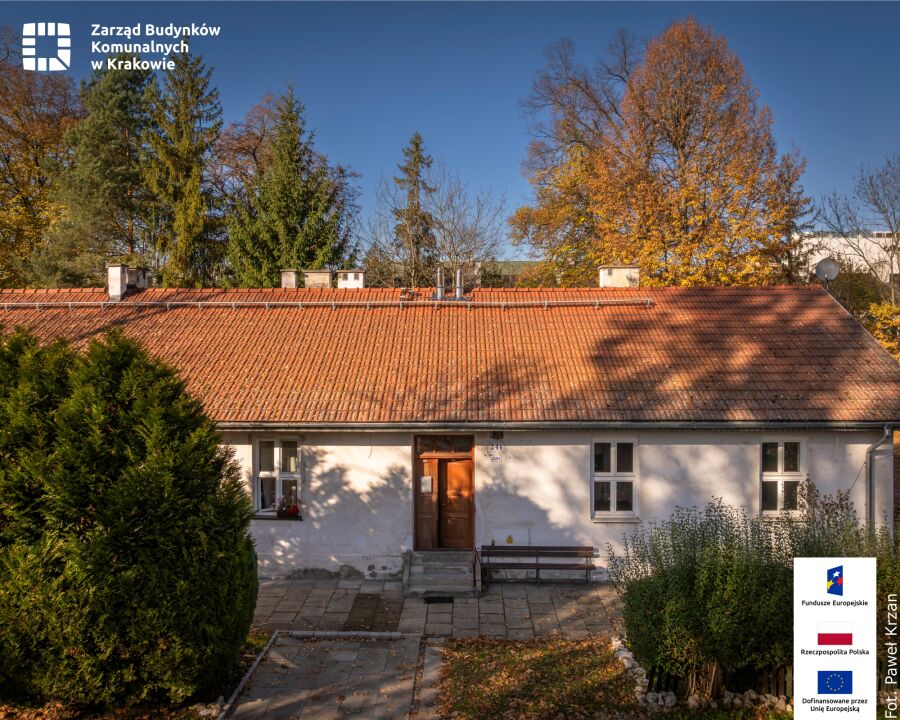 Na zdjęciu widać parterowy, biały budynek mieszkalny z dachem pokrytym czerwonymi dachówkami. Na środku fasady znajduje się drewniane wejście z niewielkimi schodkami, po bokach trzy okna.