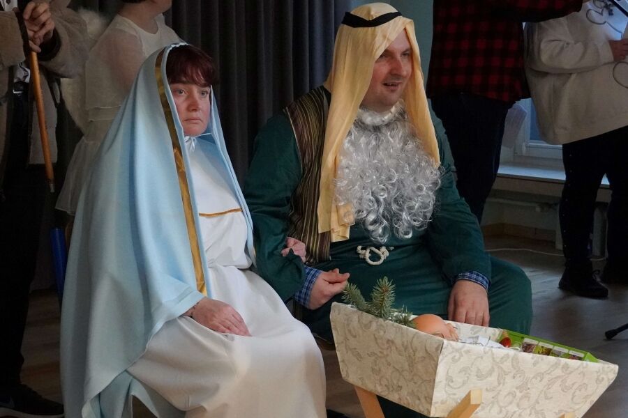 dwie osoby przebrane za maryję i józefa siedzą przed kołyską z dzieckiem