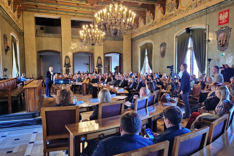 sala konferencyjna wypełniona osobami siedzącymi w półokręgu w fotelach