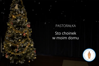 Udekorowana choinka bożonarodzeniowa z lampkami i złotymi ozdobami stoi po lewej stronie na tle ciemnej kurtyny; po prawej stronie widoczny napis „Pastorałka – Sto choinek w moim domu”.