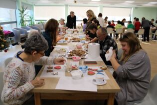 Uczestnicy warsztatów dekorują pierniki kolorowym lukrem przy długim stole w jasnej, przestronnej sali.