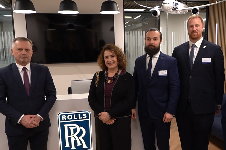 Otwarcie centrum kompetencyjnego firmy Rolls-Royce w Krakowie. Na zdjęciu wykonanym w przestrzeni biurowej w korytarzu na pierwszym planie stoją cztery osoby, trzej mężczyźni i kobieta.  