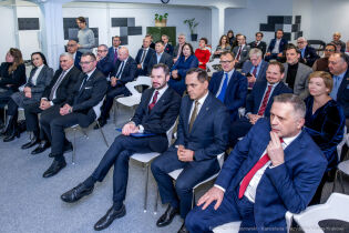 na zdjęciu kilkudziesięcioosobowa elegancko ubranych osób siedzi na białych konferencyjnych krzesłach w industrialnym wnętrzu sali. W pierwszym rzędzie po prawej Prezydent Krakowa. 