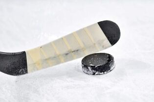 Grafika przedstawia łopatkę kija hokejowego oraz krażek hokejowy na tafli lodowiska.