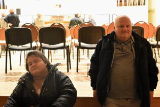 Dwie osoby stoją na pierwszym planie w sali koncertowej z ustawionymi rzędami krzeseł; w tle widać innych uczestników oraz organy na scenie.