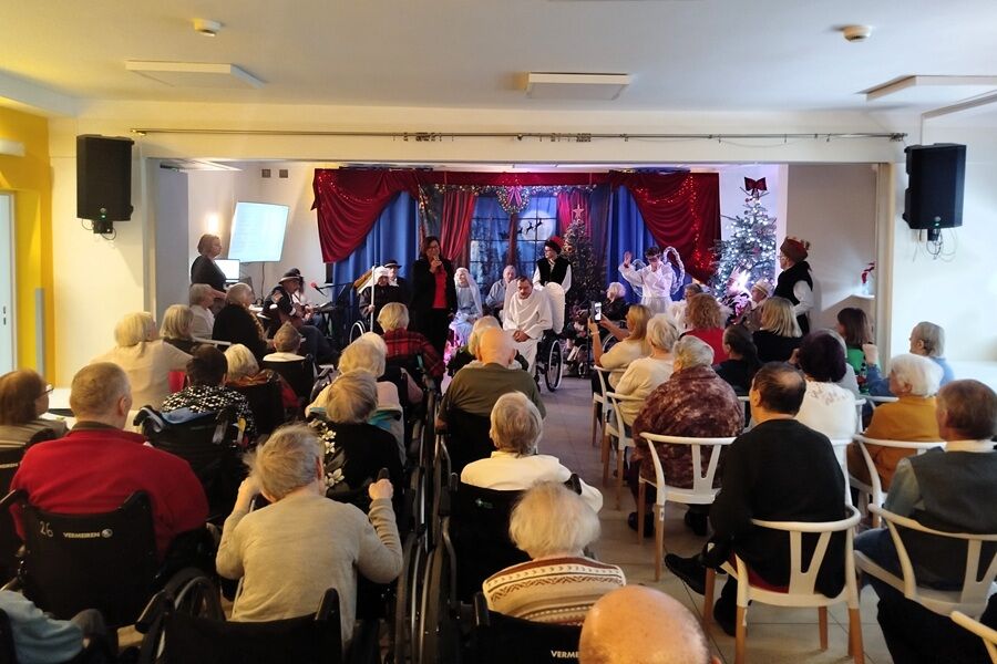 Widok na salę wypełnioną seniorami; na scenie odbywa się przedstawienie jasełkowe z udziałem aktorów w strojach, publiczność ogląda występ.