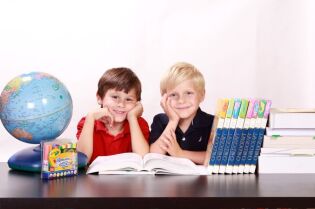 Grafika przedstawia dwoje uśmiechniętych dzieci w otoczeniu książek i przyborów szkolnych.