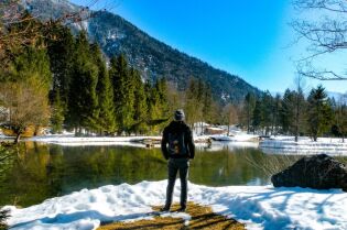 Grafika przedstawia postać stojącą na brzegu zbiornika wodnego.