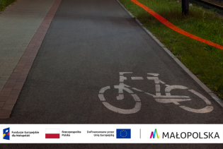Grafika przedstawia ścieżkę rowerową oraz zawiera logo programu Fundusze Europejskie dla Małopolski 2021–2027, flagę Rzeczypospolitej Polskiej, flagę Unii Europejskiej oraz znak Województwa Małopolski