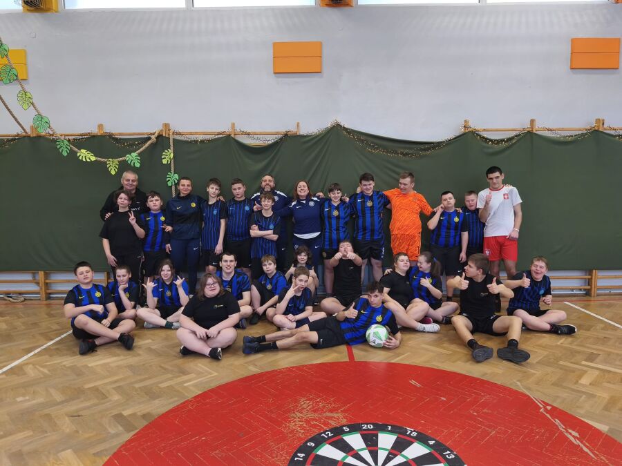 Projekt Inter Campus w Krakowie. Zdjęcie grupowe kilkunastu młodych osób oraz kilkorga dorosłych. Stoją w dwóch rzędach po drabinkami w sali gimnastycznej w koszulkach sportowych. 
