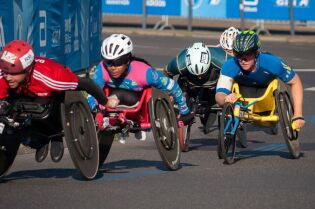 Grafika przedstawia grupę sportowców, biorących udział w wyścigach na wózkach inwalidzkich.