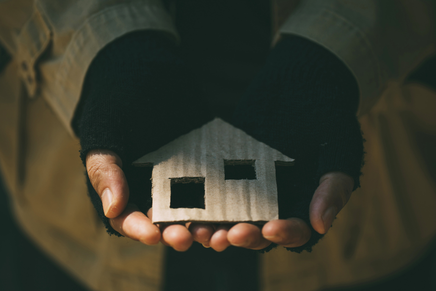 Ręce bezdomnego trzymające domek z tektury 