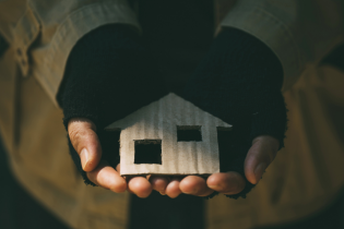 Ręce bezdomnego trzymające domek z tektury 