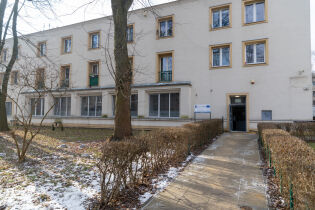 Budynek nowo otwartego Centrum dla Rodzin na Os. Krakowiaków. Widać fasadę białego budynku, chodnik, drzewa oraz śnieg.