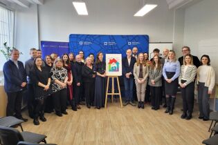 grupa osób stoi w kilku rzędach. po środku stoi na sztaludze logo centrum dla rodzin w formie kolorowego domku.