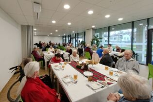 Na zdjęciu Mieszkańcy, pracownicy oraz goście siedzą przy stołach podczas wspólnej Wigilii. 