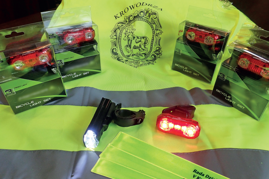 na grafice widnieje kamizelka odblaskowa z logo Krowodrzy oraz światełka odblaskowe 