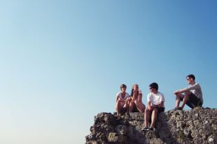 Grafika przedstawia kilka młodych osób, siedzących na skale.