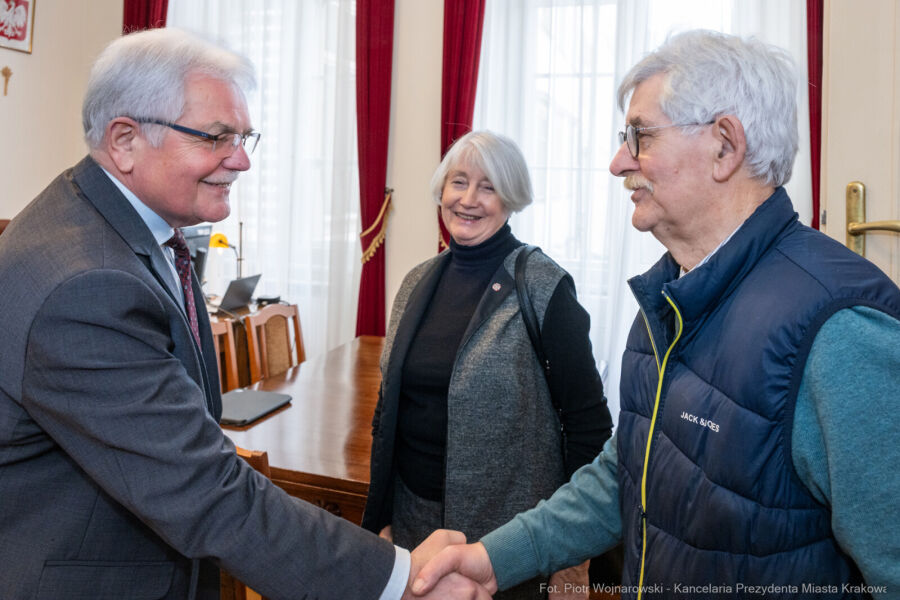 François Daubin po prawej stronie wita się przez podanie ręki z Zastępca Prezydenta Krakowa Stanisławem Kracikiem w jego gabinecie w tle stoi uśmiechnięta kobieta z siwymi włosami.         