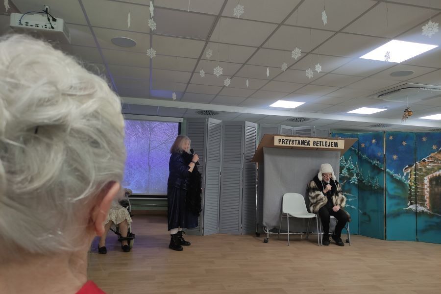 Na zdjęciu Mieszkanka patrzy na dwoje osób w dialogu przy „Przystanku Betlejem” w programie Jasełek wykonywanym przez DPS Łanowa 41.